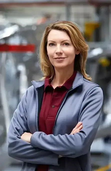 A smiling and proud girl wearing a grey blazer over a red shirt, standing in front of industrial equipment.